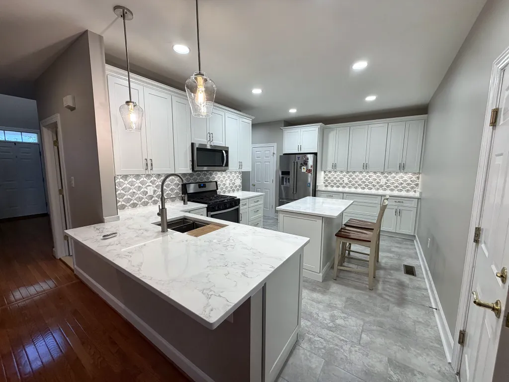 White kitchen with a quartz peninsula, glass pendants and an island